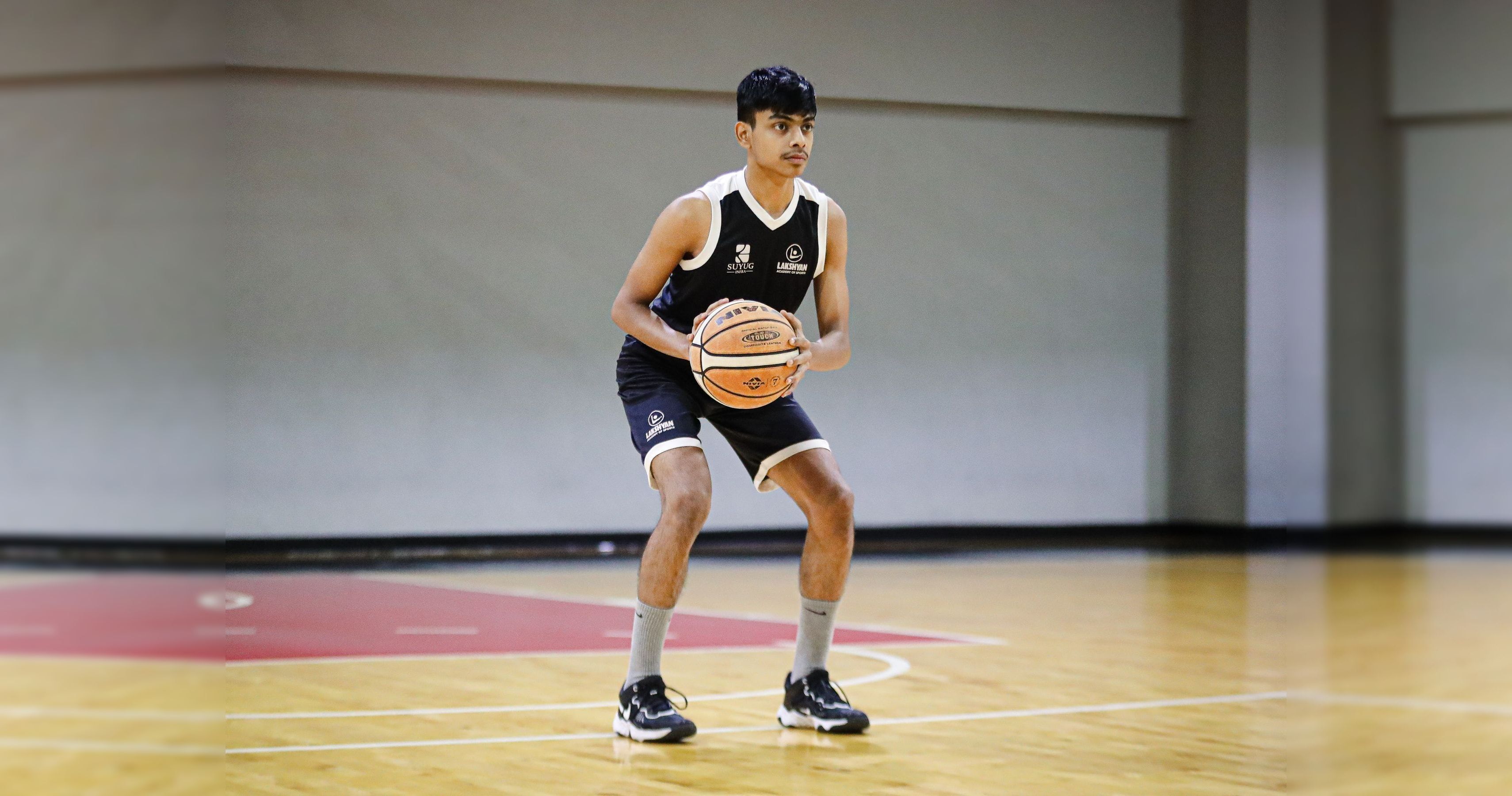 A young athlete holding a basketball on the indoor court at Lakshyan Academy of Sports