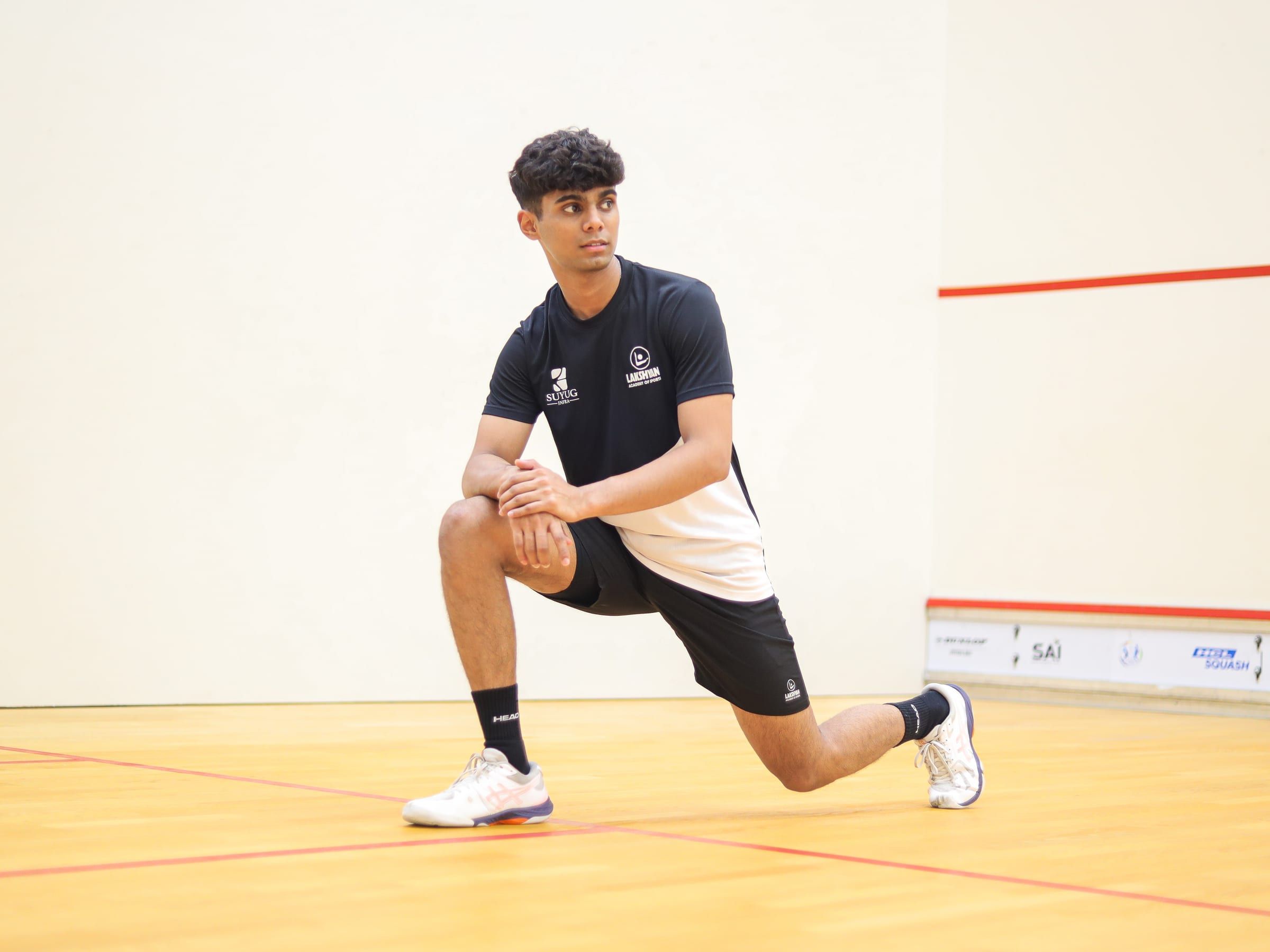A teenage athlete holding a deep lunge stretch on the squash court