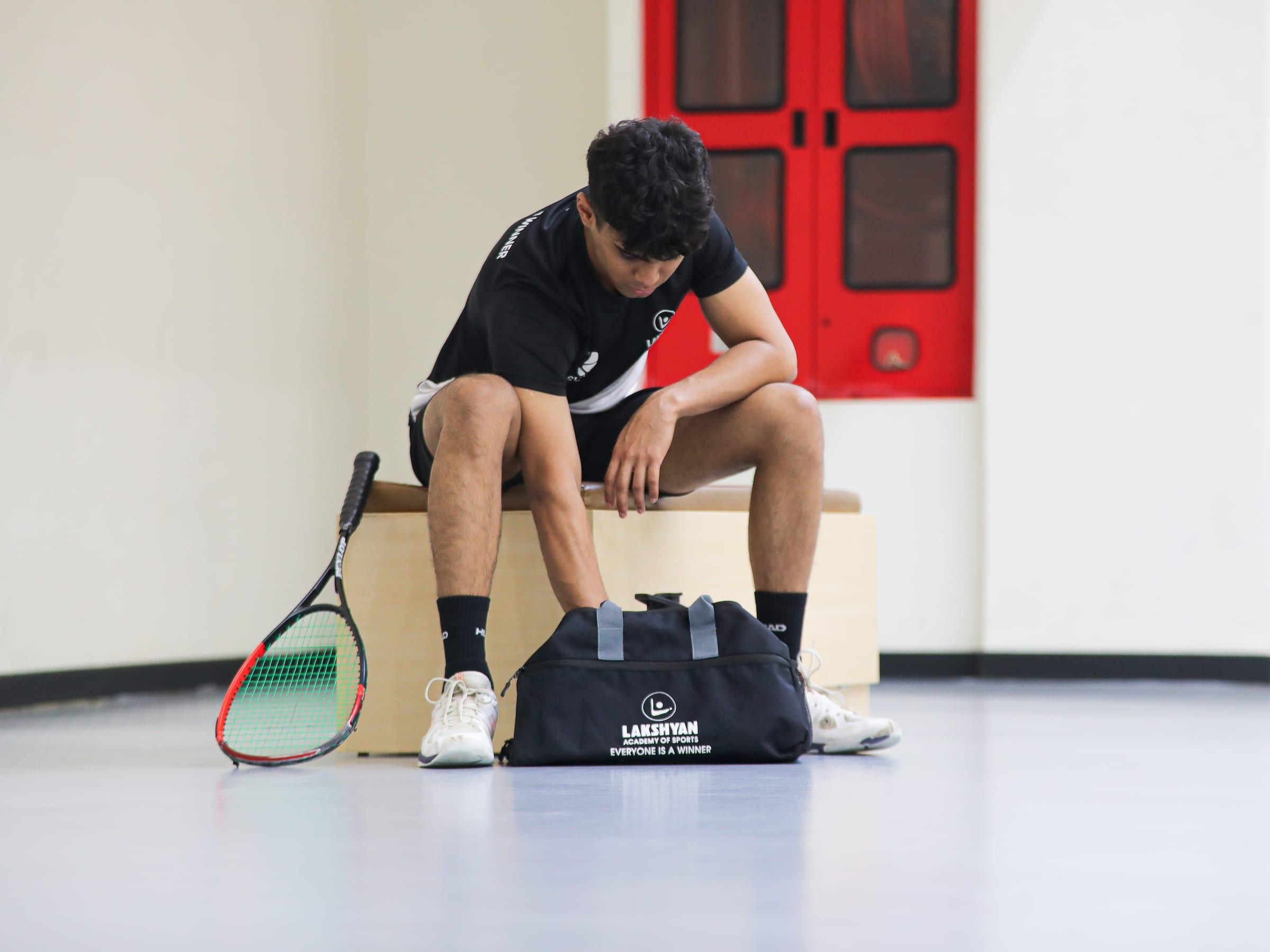 A player seated with racket and kit bag