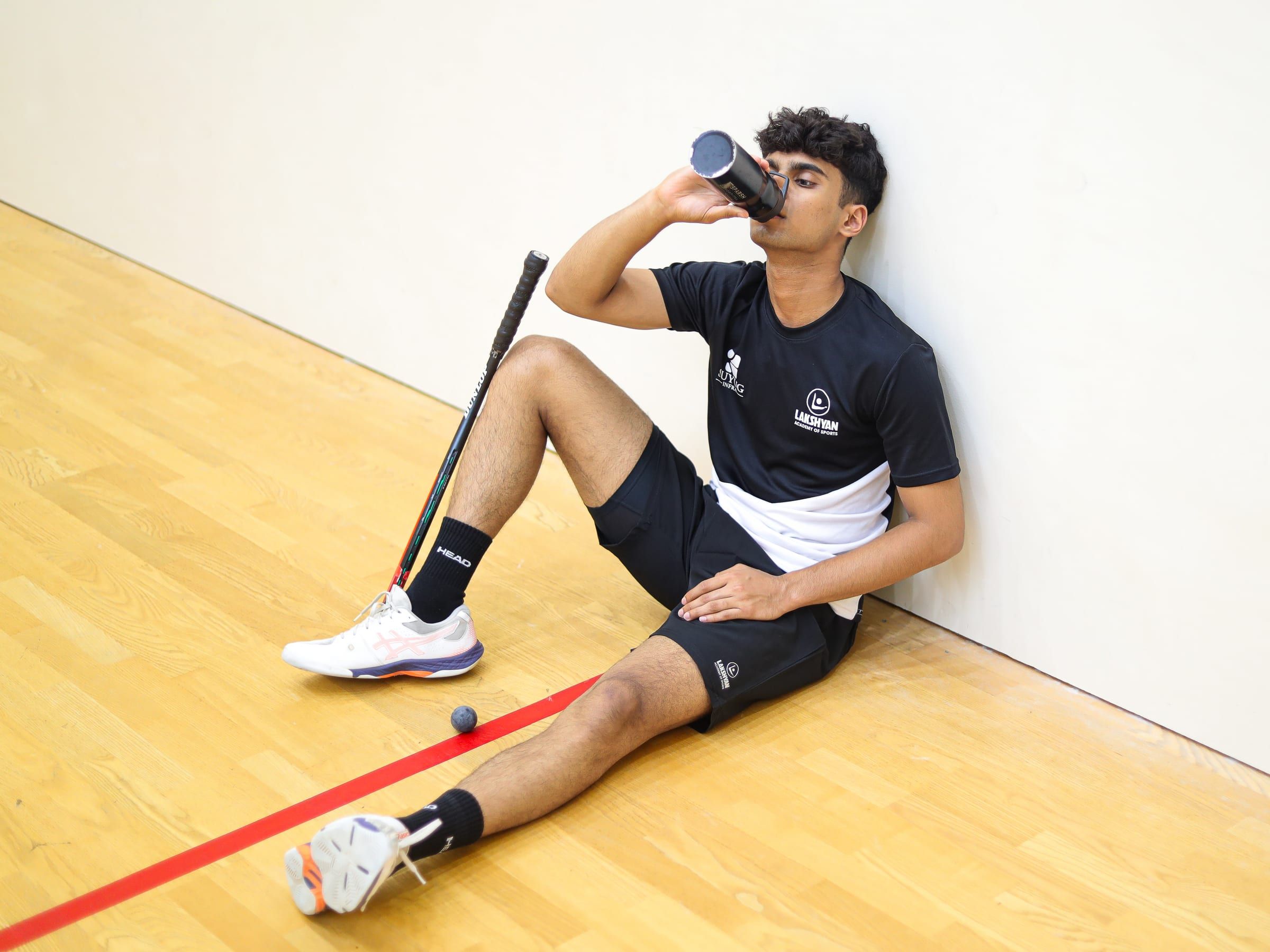 A player resting against the squash court wall with a water bottle