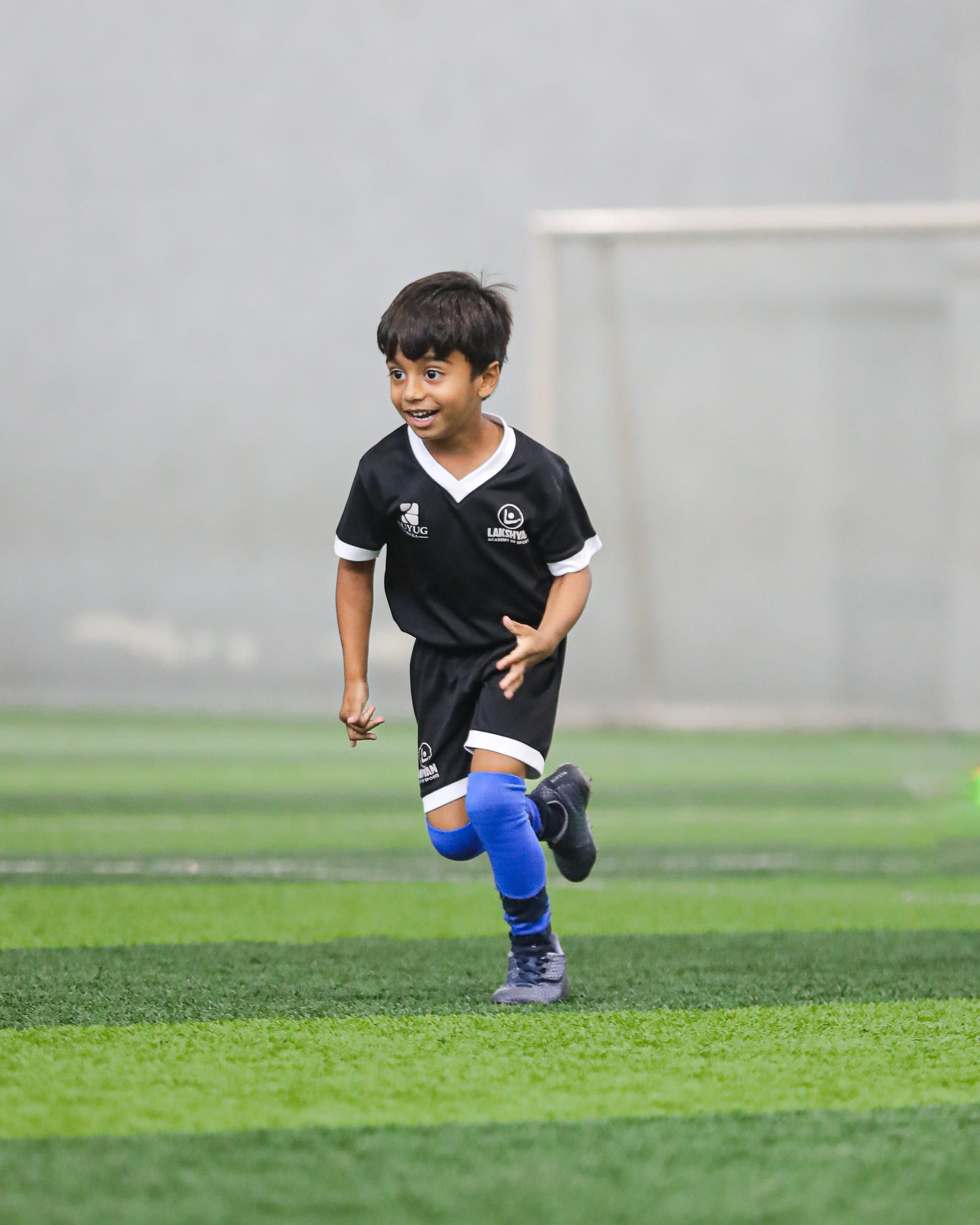 A young child running on the football pitch in Lakshyan kit